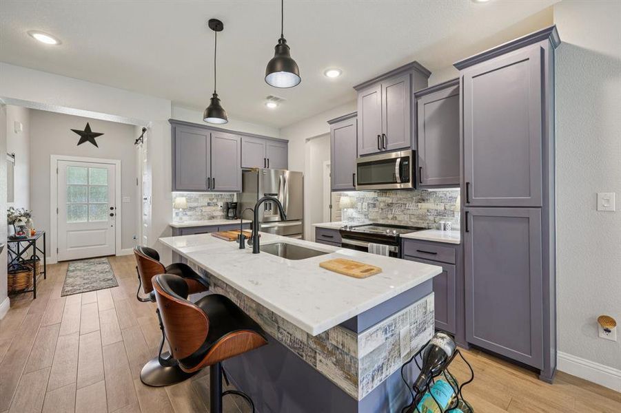 Kitchen with backsplash, light stone countertops, gray cabinets, hanging light fixtures, and a breakfast bar Kitchen with backsplash, light stone countertops, gray cabinets, hanging light fixtures, and a breakfast bar
