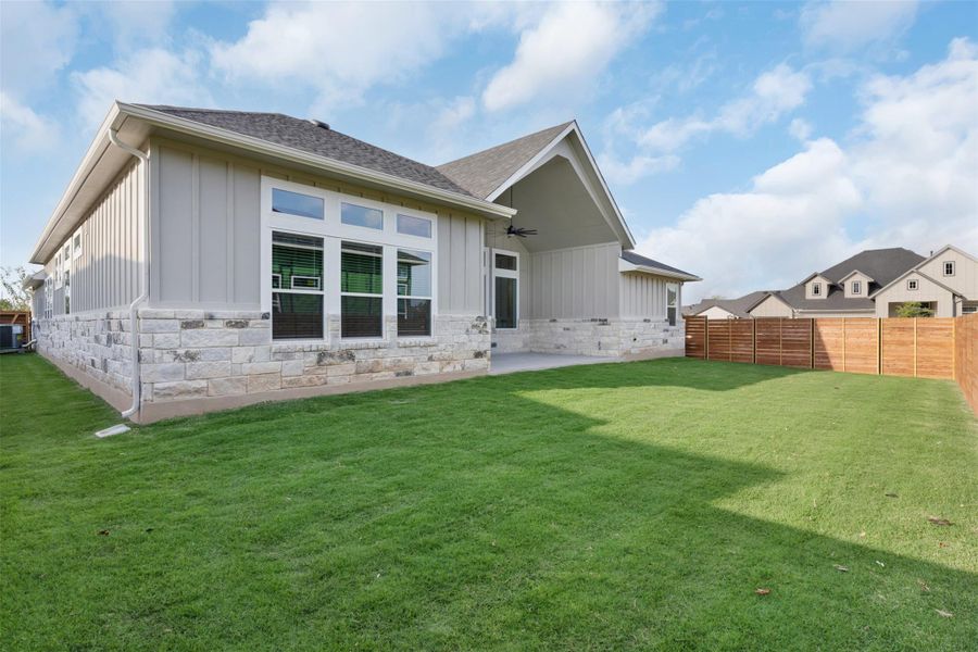 Rear view of house featuring board and batten siding, a patio area, stone siding, and ceiling fan