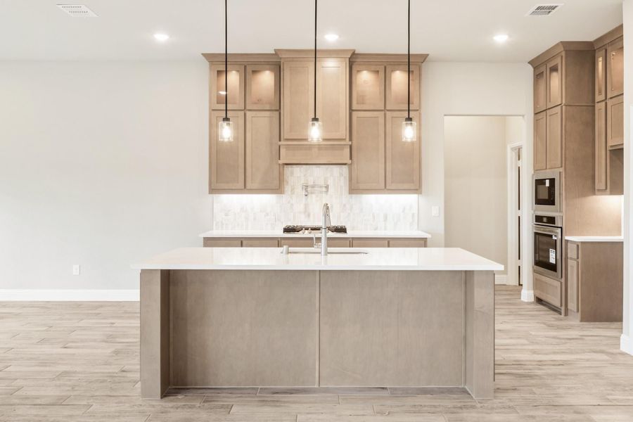Kitchen with large center island, tan wood cabinets, white countertops, and three pendant lights over the island.