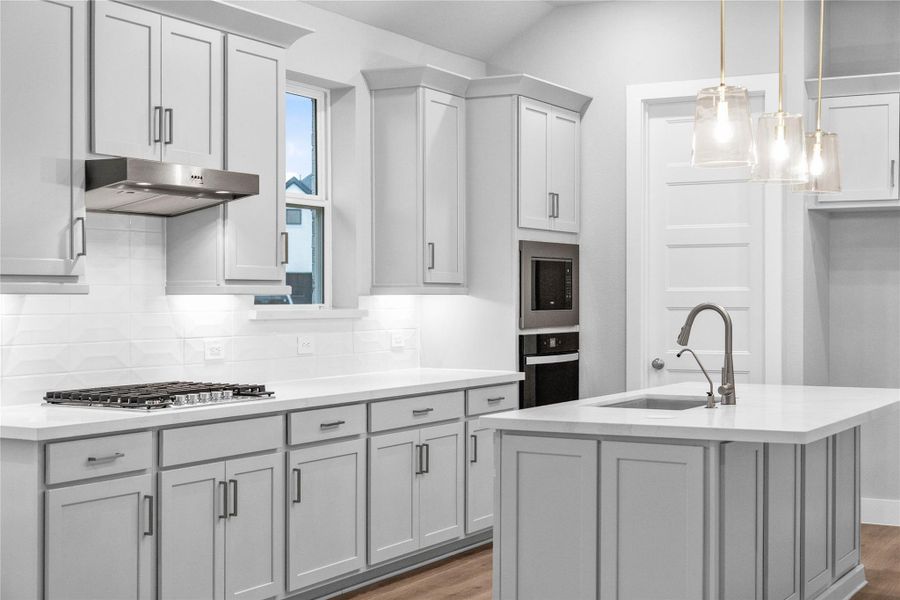 Pictured here is the Whirlpool 30-inch stainless steel gas cooktop and vent hood. The stylish white backsplash tile extends from the countertop to the upper cabinets, adding texture and visual interest.