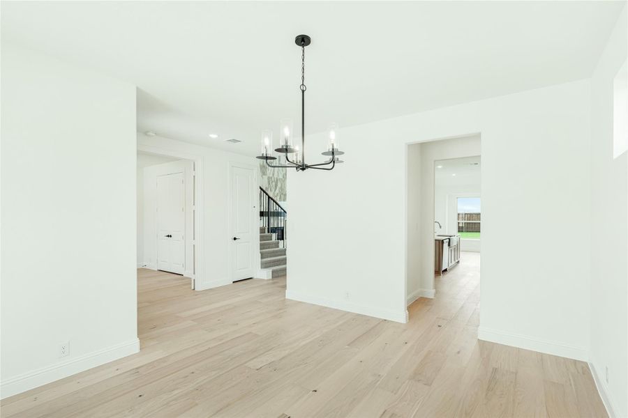 Dining area with black chandelier, light hardwood floors, and open view to staircase and kitchen