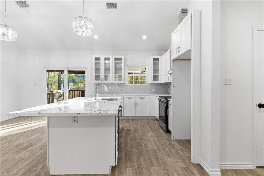Kitchen with white cabinets, glass insert cabinets, tasteful backsplash, light wood-style flooring, and pendant lighting