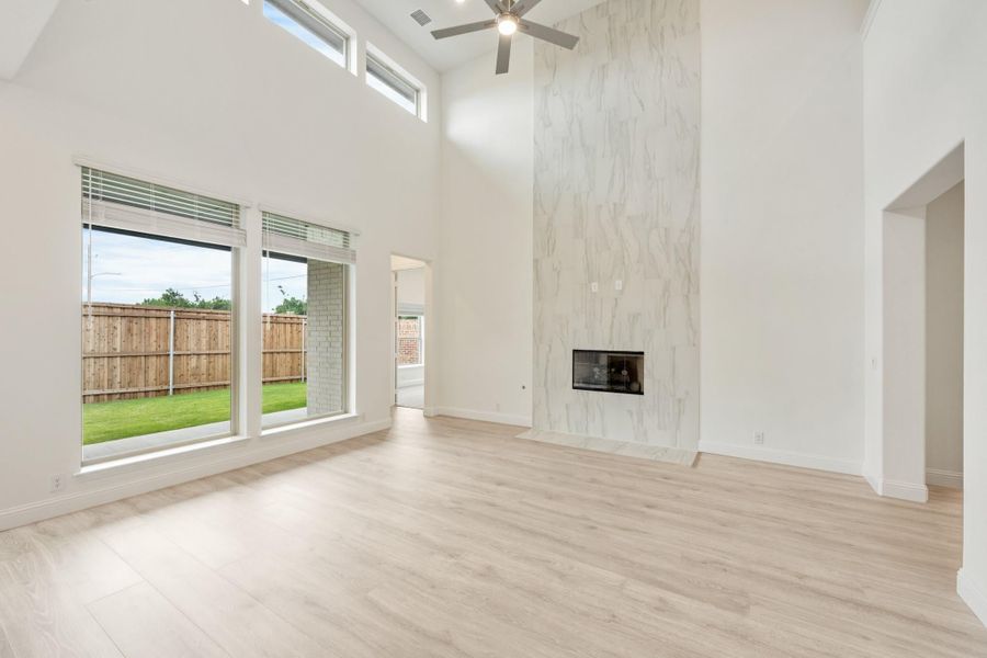 Open living room with two-story ceiling, marble fireplace surround, and light wood floors
