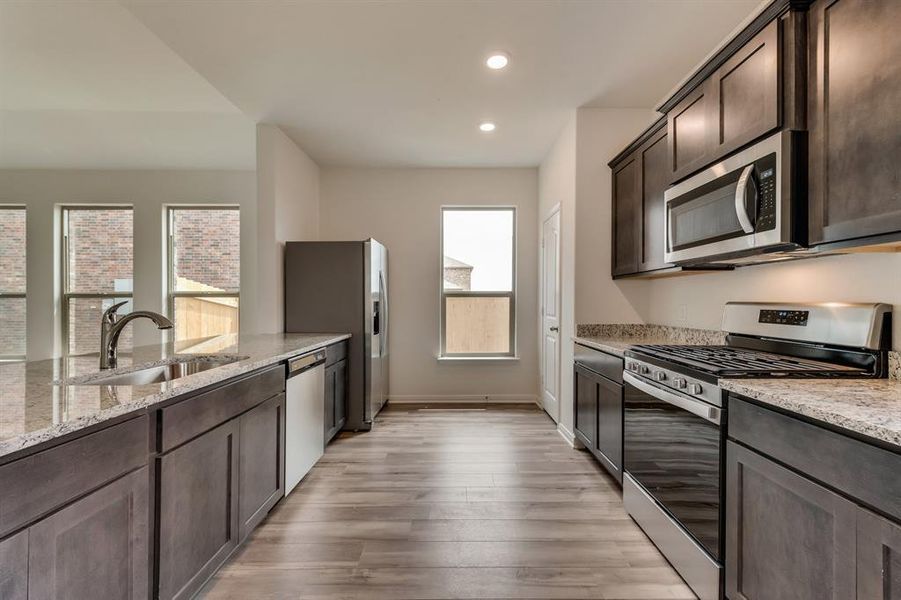 Kitchen featuring appliances with stainless steel finishes, light stone countertops, dark brown cabinets, and light wood-type flooring