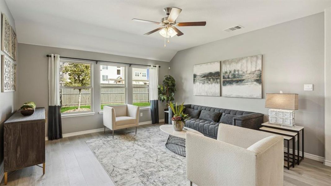 The living area features light-toned flooring, three windows with views of the backyard, and a ceiling fan