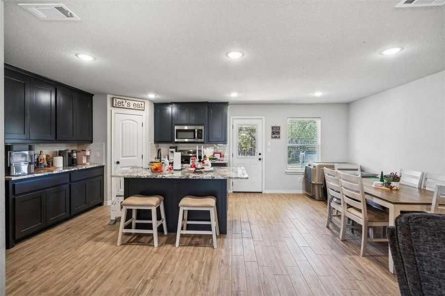 Kitchen with light stone counters, a breakfast bar, stainless steel appliances, light hardwood / wood-style floors, and a kitchen island