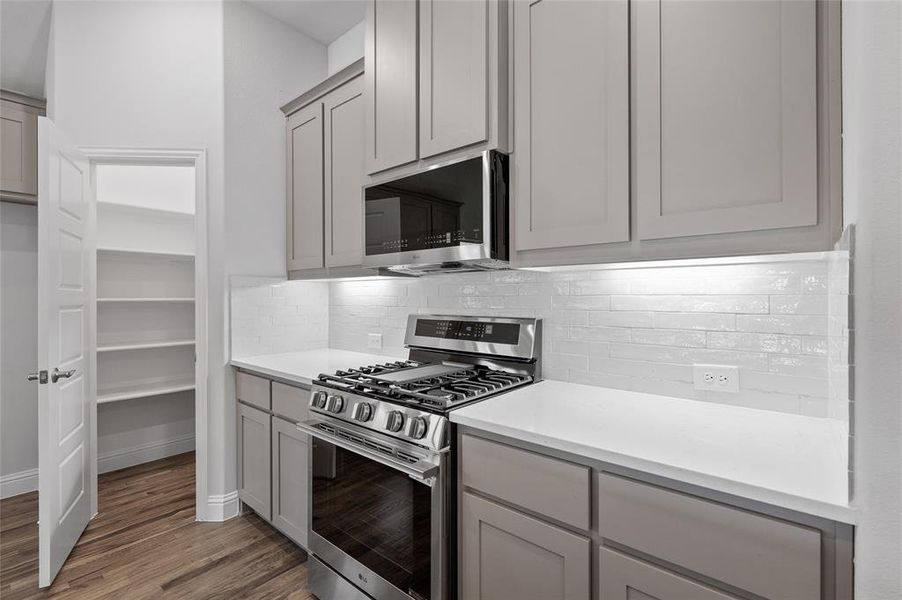 Kitchen with appliances with stainless steel finishes, gray cabinets, backsplash, and light wood-style floors