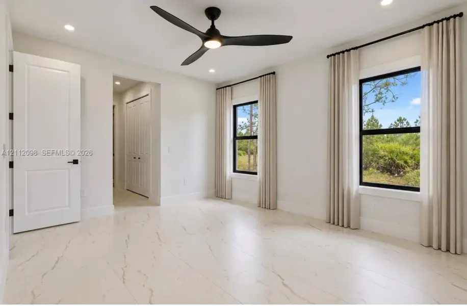 Large-format tile flooring, recessed ceiling lighting, three-blade matte black ceiling fan, and black-framed windows with exterior natural scenery Large-format tile flooring, recessed ceiling lighting, three-blade matte black ceiling fan, and black-framed windows with exterior natural scenery