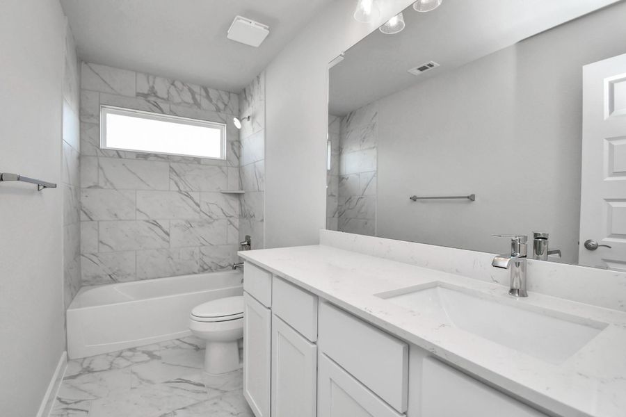 Secondary bath features tile flooring, bath/shower combo with tile surround, light stained wood cabinets, beautiful light countertop. Sample photo of completed home with similar floor plan. Actual colors and selections may vary.