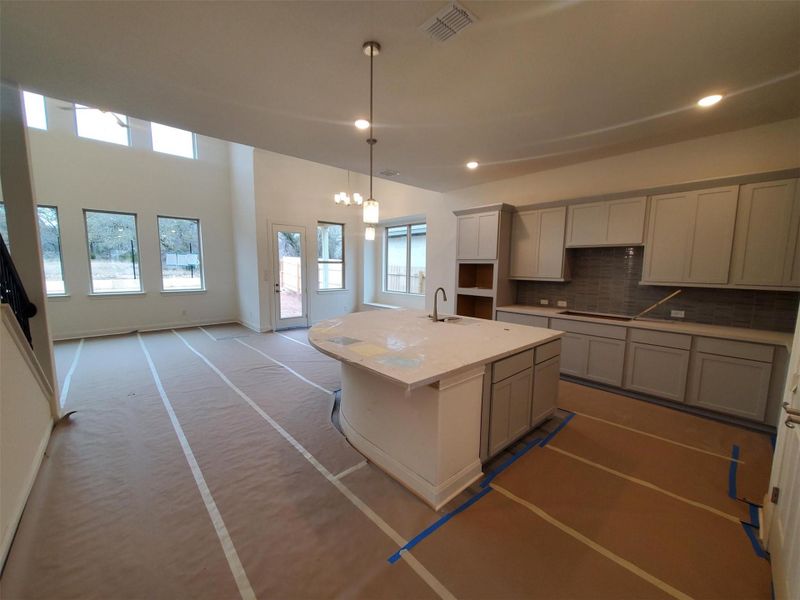 Kitchen with cooktop, sink, a center island with sink, pendant lighting, and backsplash