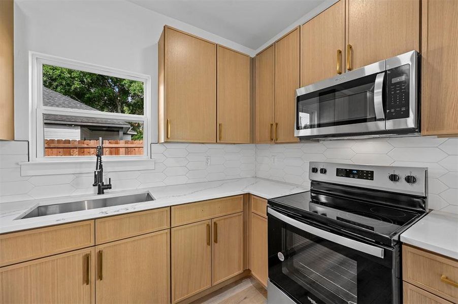 Kitchen with appliances with stainless steel finishes, sink, tasteful backsplash, and light stone countertops