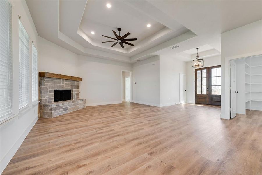 Unfurnished living room featuring french doors, a raised ceiling, light hardwood / wood-style flooring, and ceiling fan with notable chandelier