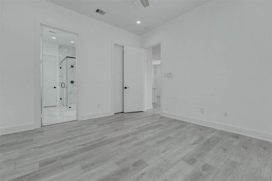 This view illustrates the direct connection between the primary bedroom and its en-suite bathroom. Clean white walls, high ceilings, recessed lighting, and uninterrupted flooring contribute to a quiet, suite-style atmosphere.