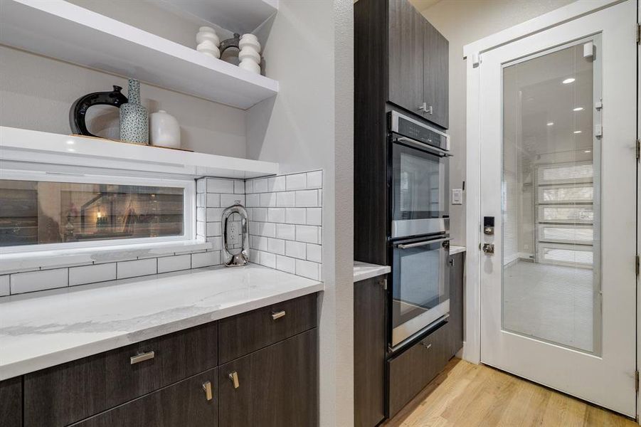 Kitchen with stainless steel double oven, light stone counters, dark brown cabinets, and light hardwood / wood-style flooring