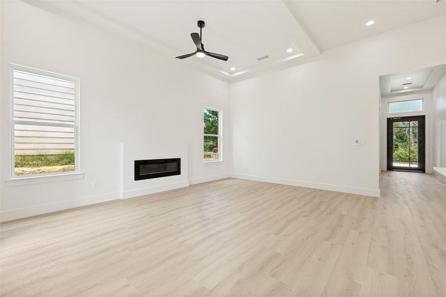 Spacious interior with light wood-finish flooring, a contemporary electric fireplace, and a black ceiling fan Spacious interior with light wood-finish flooring, a contemporary electric fireplace, and a black ceiling fan