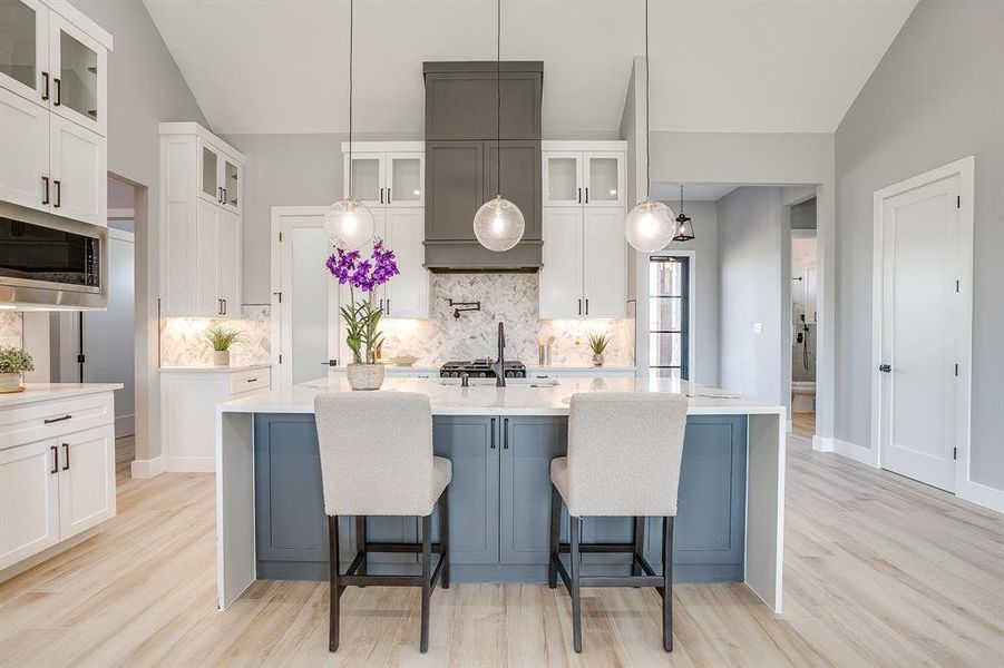Kitchen with glass insert cabinets, light stone counters, light wood-type flooring, stainless steel microwave, and white cabinets