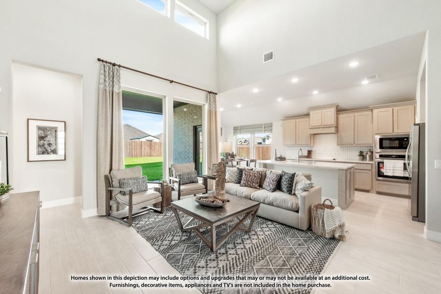 Open-concept living room with two-story ceilings, gray sofa, and kitchen visible in background