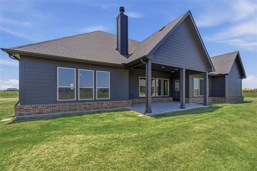 Expansive green lawn surrounds a modern residence featuring dark siding and a prominent covered patio with supporting columns Expansive green lawn surrounds a modern residence featuring dark siding and a prominent covered patio with supporting columns
