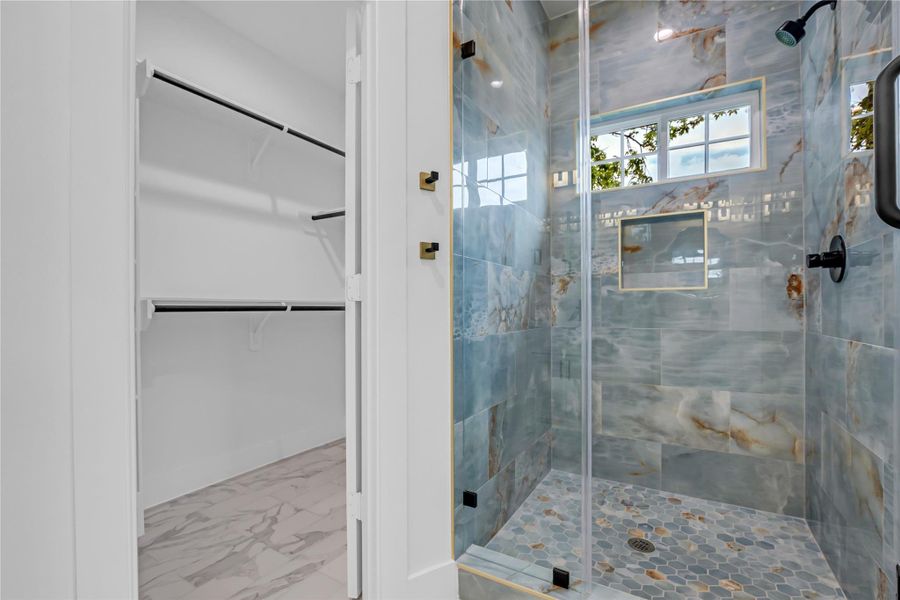 Experience luxury in this primary bathroom, featuring a stunning, modern shower with striking tile work and an adjacent spacious walk-in closet for ultimate convenience.