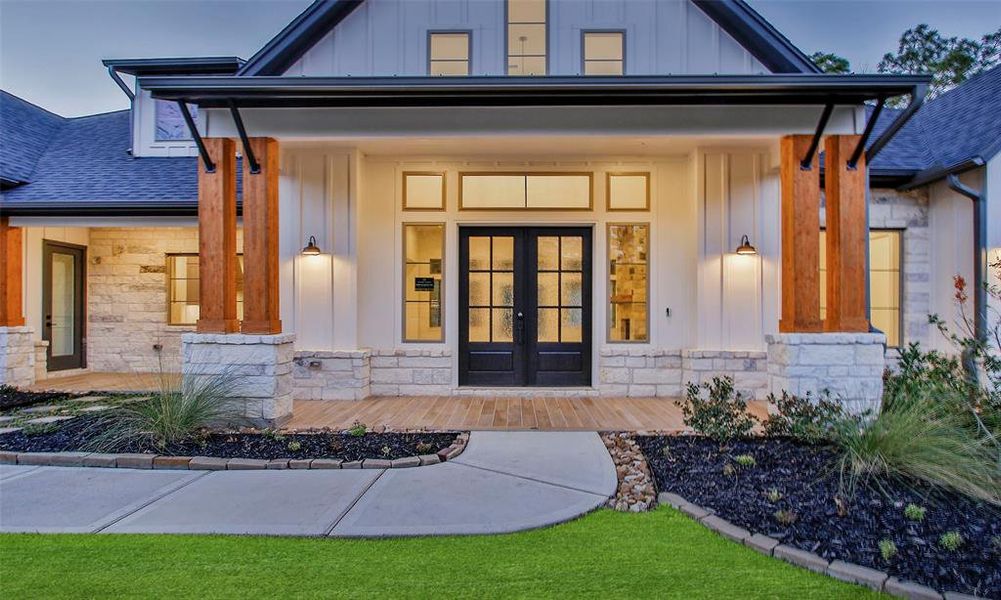 This photo showcases a darling, inviting entrance with a mix of stone and wood accents. It features large double doors, elegant lighting, and a well-maintained front yard with landscaped greenery.