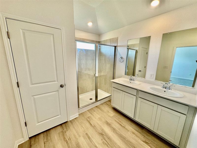 Full bath featuring a shower stall, double vanity, and light wood-type flooring Full bath featuring a shower stall, double vanity, and light wood-type flooring