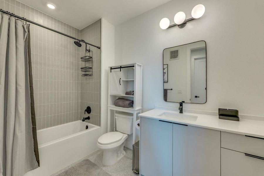 The bathroom features a white vanity with a white countertop and a rectangular undermount sink, a large mirror with a black frame, and a bathtub with light gray subway tile walls