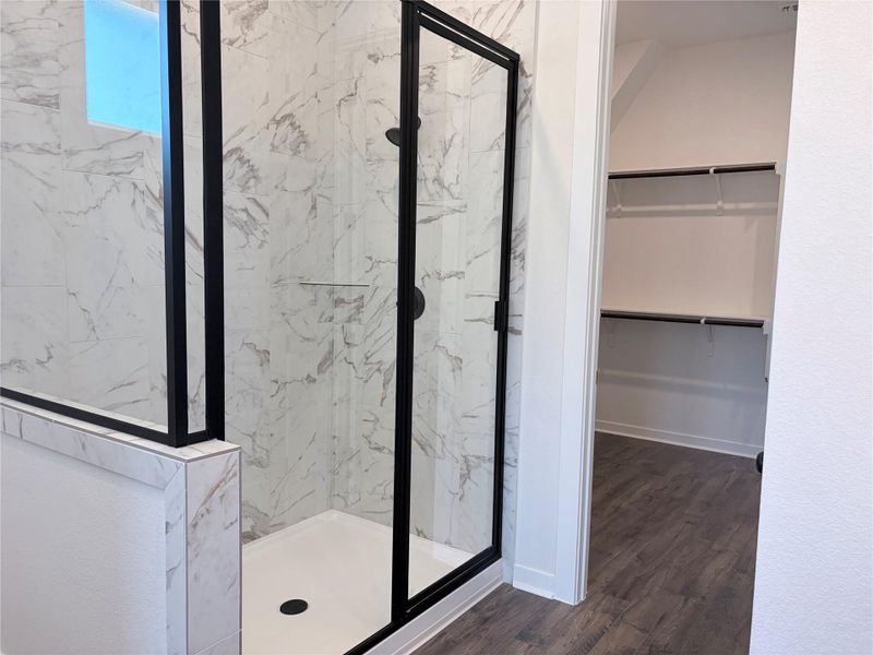 Marble-patterned tile lines the walk-in shower situated adjacent to a spacious closet with built-in shelving. Marble-patterned tile lines the walk-in shower situated adjacent to a spacious closet with built-in shelving.