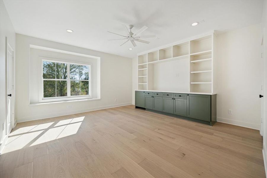 The expansive game room offers built-in storage with deep green cabinetry and open shelving, blending practicality with style. A large picture window creates a cozy sitting nook while providing a serene view. Spacious enough for entertaining or relaxing, the layout allows for flexible use of the area.