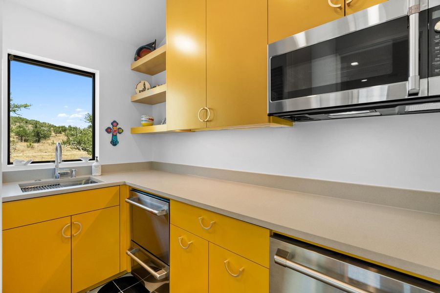 Kitchenette with vibrant yellow cabinetry, light-toned countertops, and a stainless steel under-mount sink