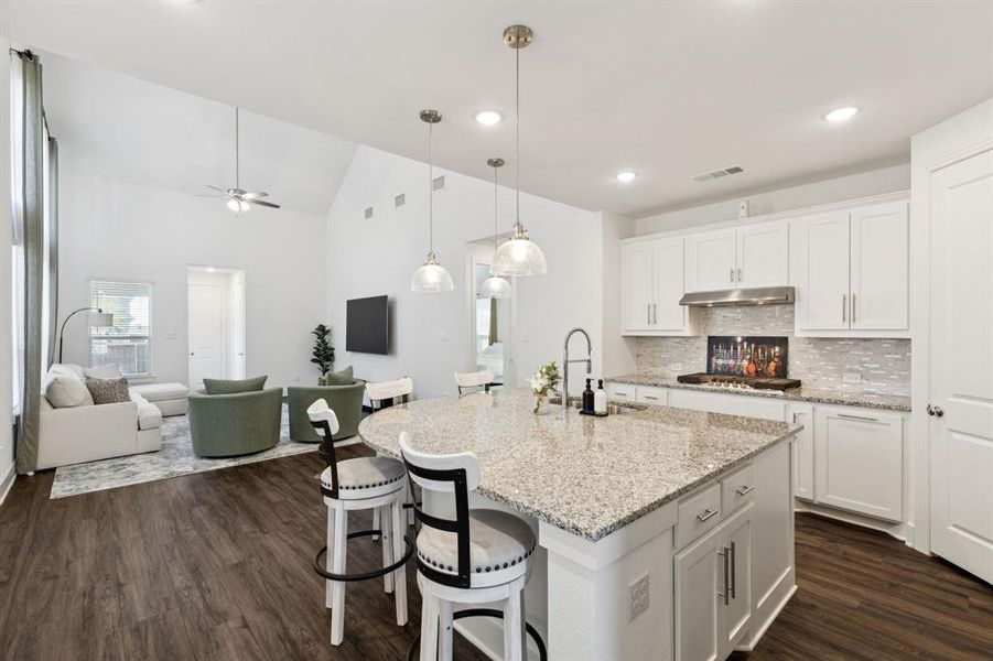 Kitchen with white cabinetry, open floor plan, decorative light fixtures, decorative backsplash, and an island with sink Kitchen with white cabinetry, open floor plan, decorative light fixtures, decorative backsplash, and an island with sink