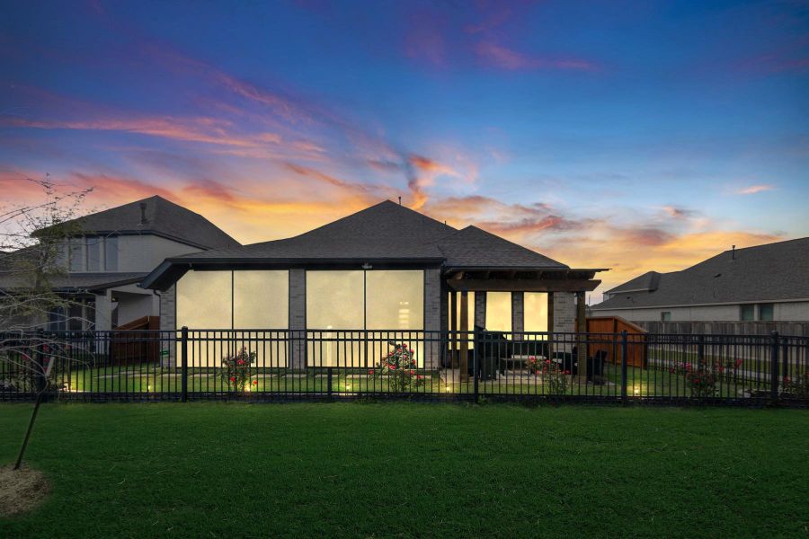 This photo showcases a modern home with a well-lit enclosed patio, a neatly manicured lawn, and a fenced backyard, set against a beautiful sunset sky. Perfect for enjoying outdoor living.