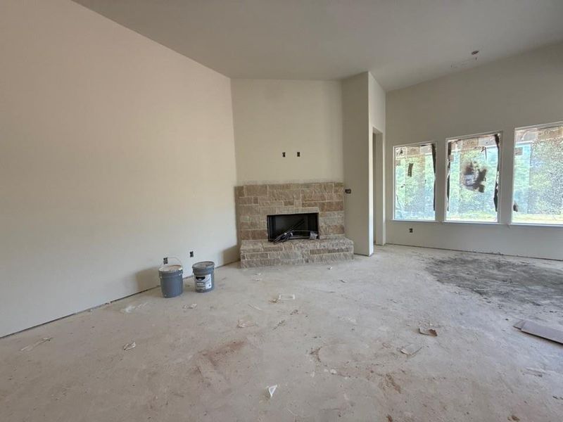 Spacious room featuring a stone fireplace with a black firebox, vaulted ceilings, and a wall of three large windows