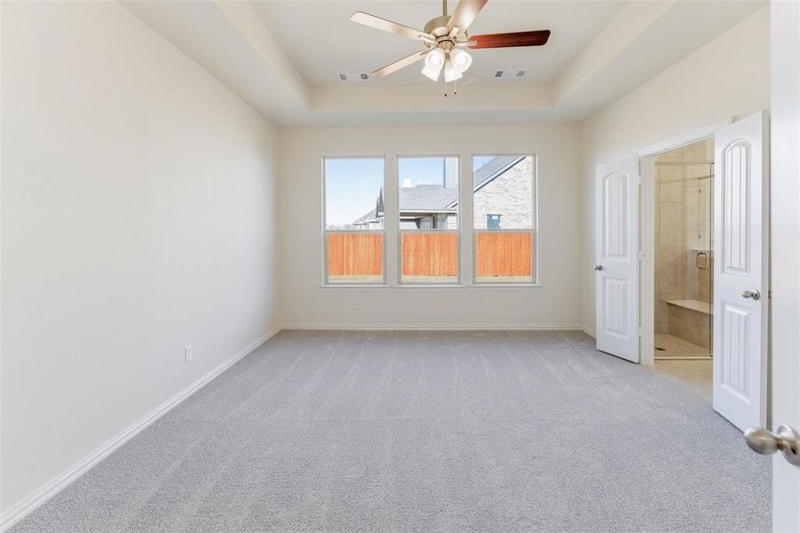 Empty room with light colored carpet, a tray ceiling, and ceiling fan Empty room with light colored carpet, a tray ceiling, and ceiling fan