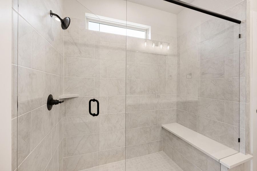 Walk-in shower with marble tile walls, built-in bench, glass door, and black fixtures Walk-in shower with marble tile walls, built-in bench, glass door, and black fixtures