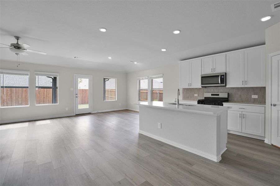 Kitchen with white cabinets, a kitchen island with sink, open floor plan, black gas range, and stainless steel microwave Kitchen with white cabinets, a kitchen island with sink, open floor plan, black gas range, and stainless steel microwave