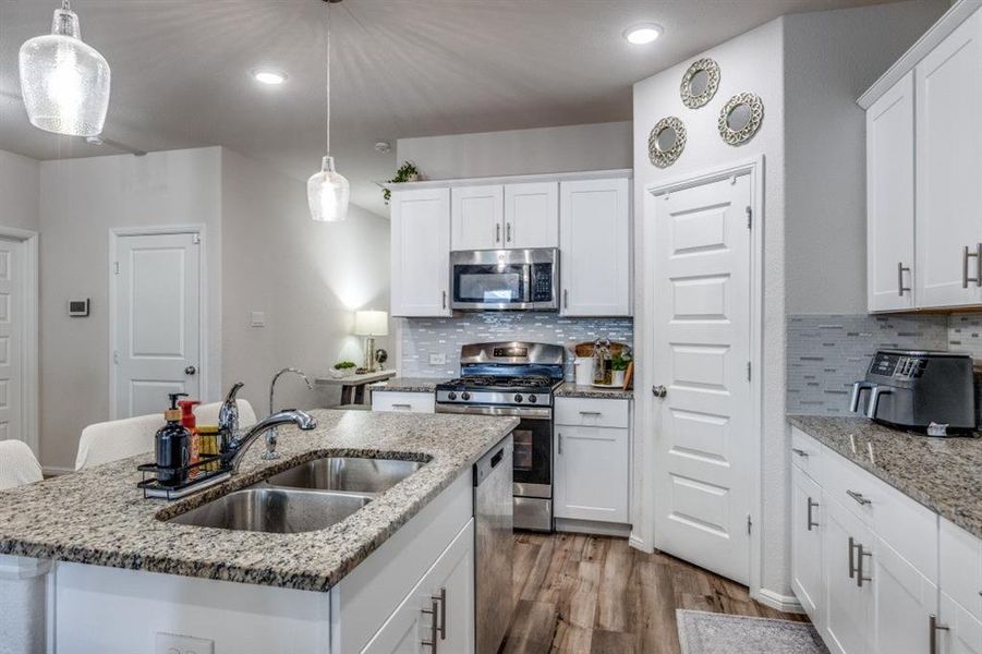 Kitchen with stainless steel appliances, white cabinets, hanging light fixtures, dark wood finished floors, and tasteful backsplash