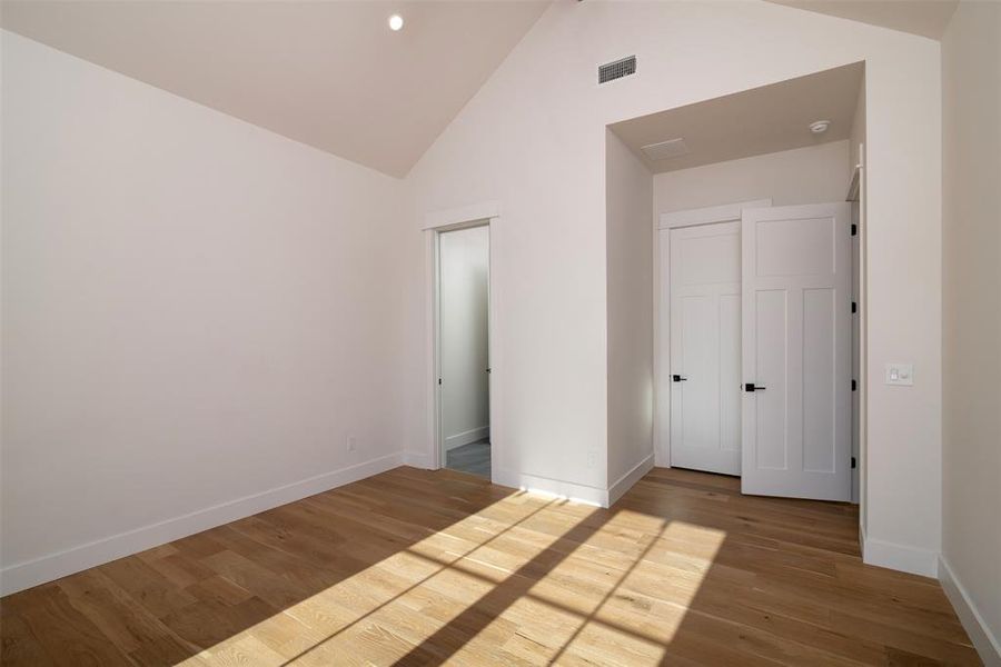 Unfurnished bedroom with a closet, hardwood / wood-style floors, and high vaulted ceiling