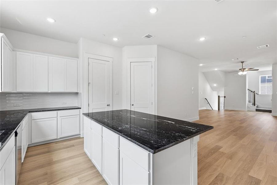 Kitchen featuring an island with a dark countertop, white cabinetry, and light wood flooring