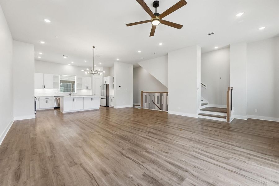 Open-concept living and kitchen area showcasing wide-plank flooring, modern ceiling fan, sleek stair railing, and a bright, spacious layout with contemporary finishes throughout.