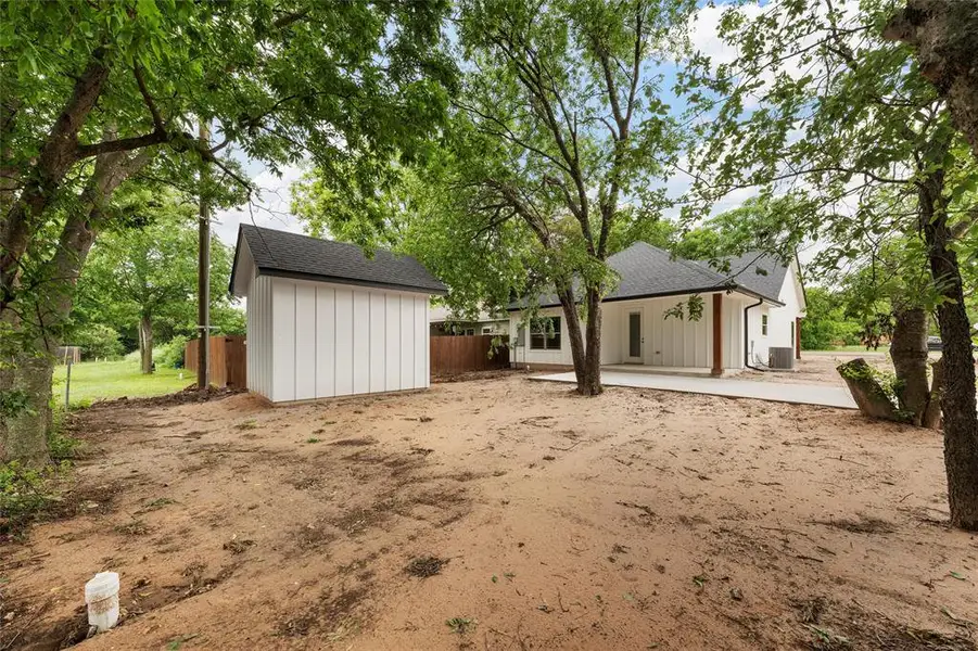 Rear view of house featuring an outdoor structure, fence, a shingled roof, a storage unit, and central air condition unit