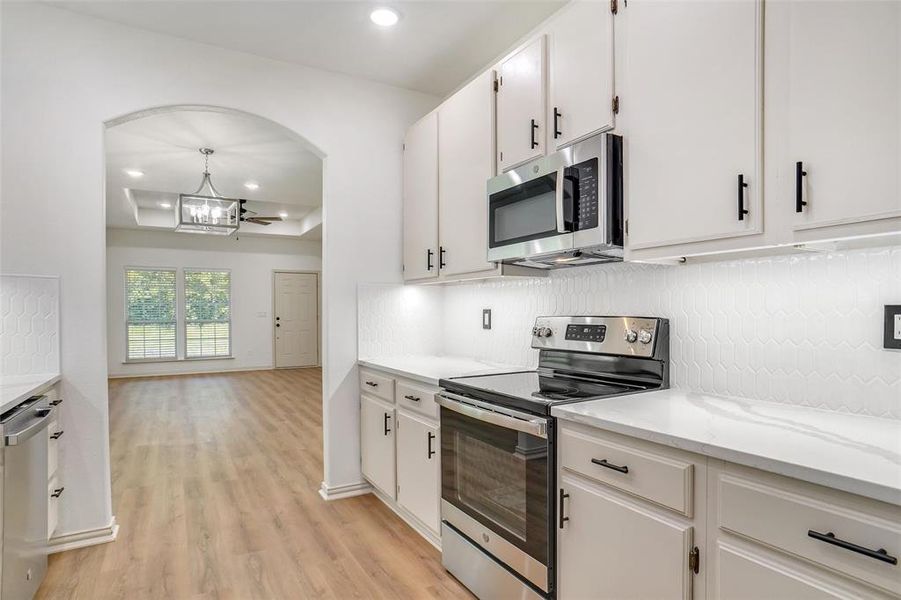 Kitchen featuring light stone counters, backsplash, appliances with stainless steel finishes, white cabinets, and light wood-type flooring