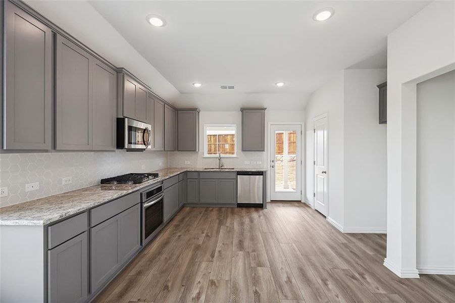 Kitchen with gray cabinetry, stainless steel appliances, dark wood-style flooring, recessed lighting, and backsplash