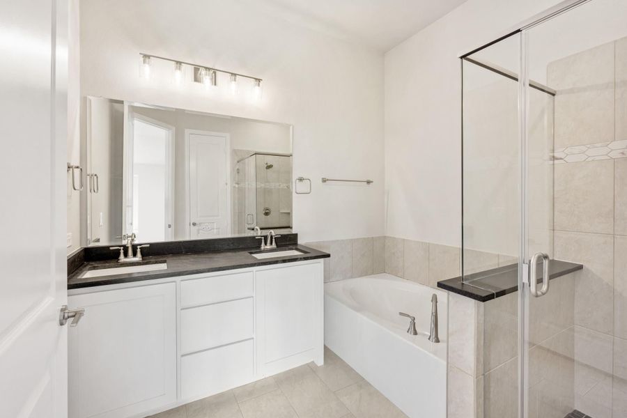 Bathroom with double sink vanity, dark countertop, soaking tub, and glass-enclosed shower with tile walls Bathroom with double sink vanity, dark countertop, soaking tub, and glass-enclosed shower with tile walls