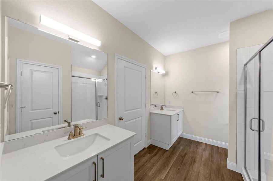 Bathroom featuring dual vanities with white cabinetry and integrated sinks, quartz-finish countertops, and wood-finish flooring