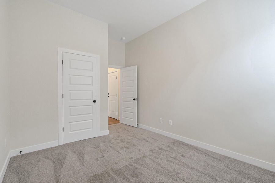 Neutral tone walls, grey textured carpeting, white baseboards, and white paneled doors with black hardware Neutral tone walls, grey textured carpeting, white baseboards, and white paneled doors with black hardware