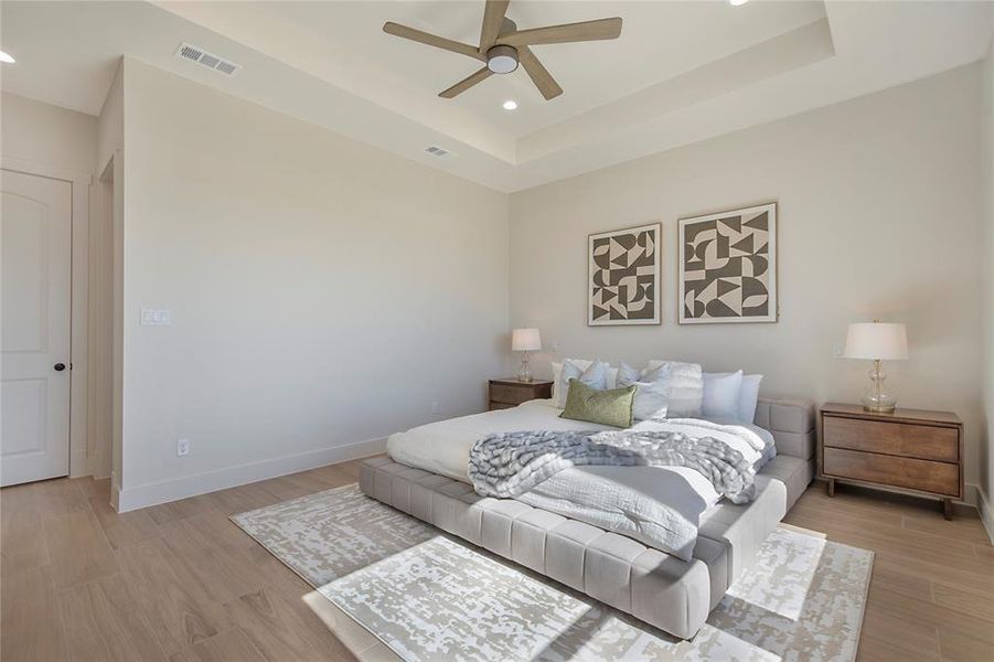 Bedroom with a raised ceiling, light wood-style flooring, recessed lighting, and a ceiling fan Bedroom with a raised ceiling, light wood-style flooring, recessed lighting, and a ceiling fan