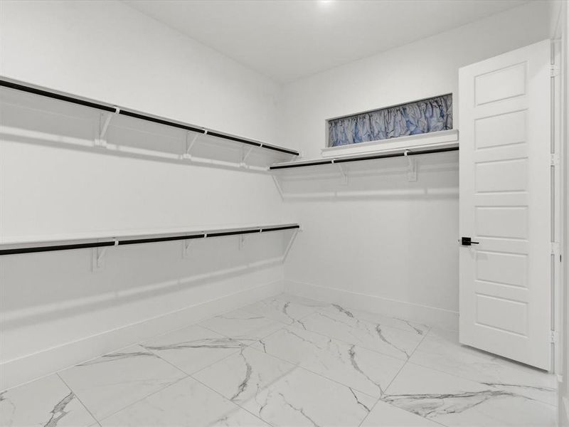 Spacious walk-in closet featuring white marble-look tile flooring, extensive built-in shelving, hanging rods, and a high horizontal window Spacious walk-in closet featuring white marble-look tile flooring, extensive built-in shelving, hanging rods, and a high horizontal window