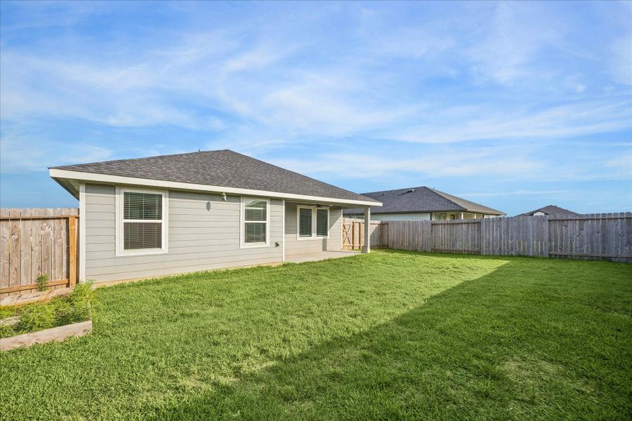 Spacious backyard with a well-maintained lawn, enclosed by a wooden fence. The covered patio features a ceiling fan, providing a comfortable outdoor space.