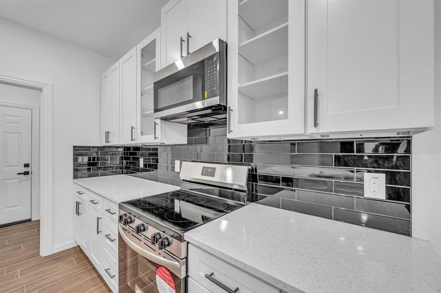 Kitchen with stainless steel appliances, tasteful backsplash, light stone countertops, and white cabinets