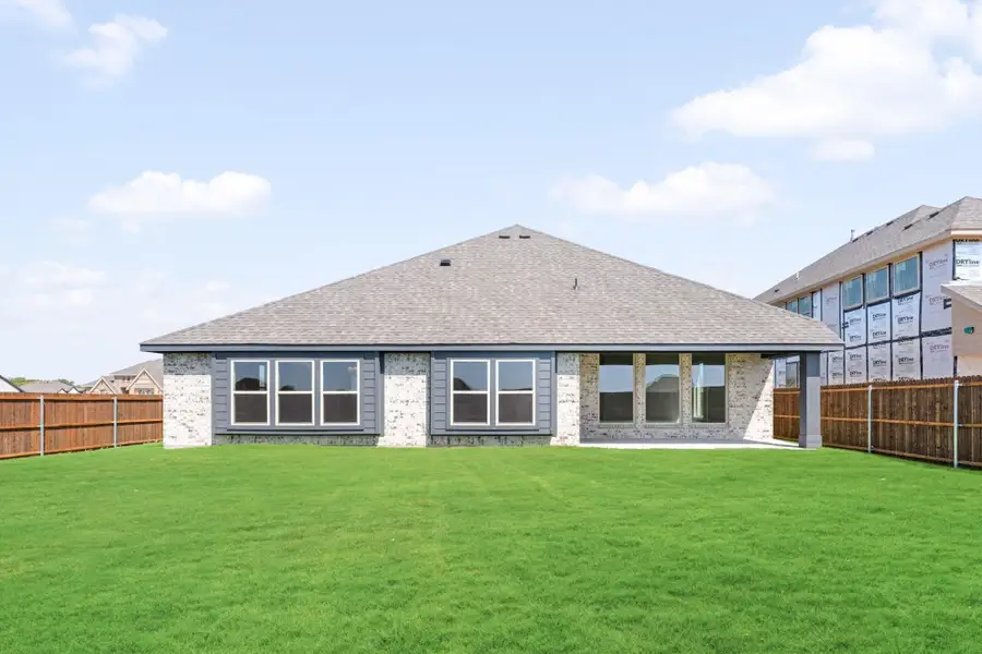 Rear exterior of single-story brick home with large windows, covered patio, and fenced backyard with green lawn.